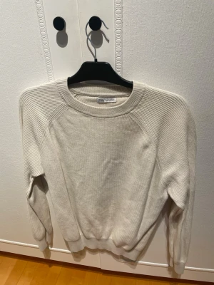 Beige stickad tröja från Zara - Säljer en stilren beige stickad tröja från Zara. Tröjan har rund halsringning, ribbade muddar och är tillverkad i ett mjukt, ribbstickat material. Perfekt för lager på lager och enkel att matcha med olika outfits.