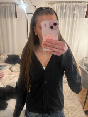 Svart v-ringad kofta med knappar - Snygg svart kofta med v-ringning och knäppning framtill. Långärmad och enkel design som passar till det mesta. Perfekt att slänga över en topp eller t-shirt för en stilren look.