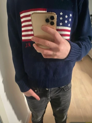 Mörkblå stickad tröja Polo Ralph Lauren - Säljer en mörkblå stickad tröja från Polo Ralph Lauren med amerikansk flagga i rött, vitt och blått på bröstet. Tröjan har rund halsringning och ribbstickade muddar vid ärmslut och nederkant. RL-broderi i rött nedtill på flaggan. priset är ganska fast 