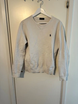 Polo Ralph Lauren sweatshirt   - Klassisk vit sweatshirt från Polo Ralph Lauren med rund halsringning och diskret broderad logga på bröstet. Tröjan har ribbade muddar vid ärmslut och nederkant samt mjuk insida för extra komfort. Perfekt för en avslappnad och stilren look.