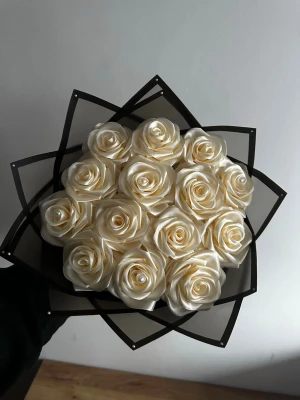 Bukett med krämvita sidenrosor - Snygg bukett med konstgjorda rosor i krämvit färg, tillverkade av glansigt sidenband. Rosorna är arrangerade i en dekorativ svart pappersinslagning som ger en modern och stilren look. Perfekt som accessoar eller dekoration till modefoton eller events.