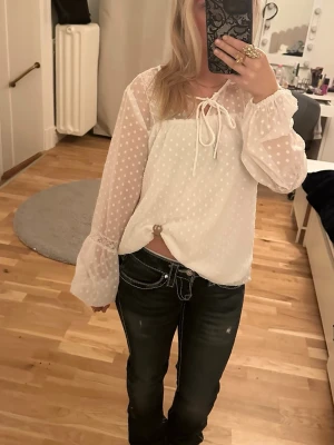 Vit prickig blus med volymärmar - Söt vit blus med diskreta prickar och transparenta volymärmar. Blusen har knytning vid halsen och är tillverkad i ett lätt, luftigt material som ger en romantisk känsla. Perfekt att styla med jeans eller kjol för en trendig look. Är i storlek 34 och passar bra för både xs och S