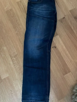 Mörkblå jeans med raka ben - Snygga mörkblå jeans med raka ben och klassisk femficksdesign. Jeansen har diskreta slitningar och kontrastsömmar som ger en cool look. Perfekta för dig som gillar en avslappnad stil. Materialet är robust denim.