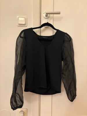 Svart blus  - Stilren svart blus med v-ringning och långa, transparenta ärmar. Står att den är i storlek L men sitter bra på mig som har för det mesta str S