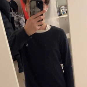 Mörkblå tröja från Polo Ralph Lauren - Snygg mörkblå tröja från Polo Ralph Lauren med klassisk rund hals och diskret logga på bröstet. Tröjan har lång ärm och är gjord i mjuk bomull, perfekt för dig som gillar stilrena och enkla plagg. Passar dig som vill ha en clean look.