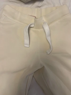 Gula mjukisbyxor med broderi - Säljer ett par krämvita mjukisbyxor med bred resår i midjan och vita dragsnören. Från Gina tricot.