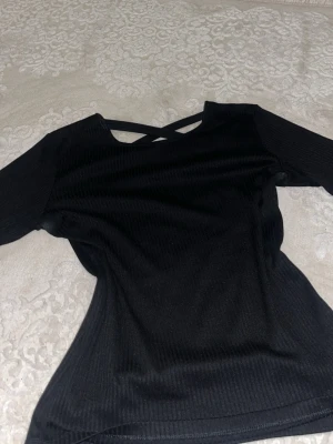 Svart ribbad topp med snörning - Snygg svart ribbad topp med långa ärmar och trendig snörningsdetalj vid baksidan av halsen. Toppen har en kroppsnära passform och är perfekt för att lyfta vilken outfit som helst. Tillverkad i mjukt och stretchigt material för extra komfort. Denna tröja passar mig utmärkt (jag har storlek S/M)