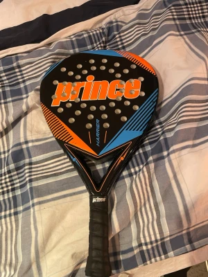 Svart och blå padelracket från Prince - Säljer en padelracket från Prince, modell Harrier. Rund form med hålmönster och greppvänligt handtag. 