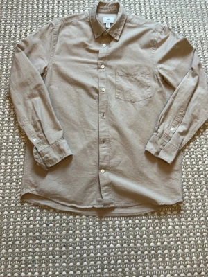 Beige skjorta från H&M med bröstficka - Stilren beige skjorta från H&M med klassisk krage, knäppning framtill och en bröstficka. Skjortan har långa ärmar med manschettknappar och är tillverkad i mjuk bomull. Perfekt för en clean och avslappnad look. Pris kan diskuteras!! Nytt skick 