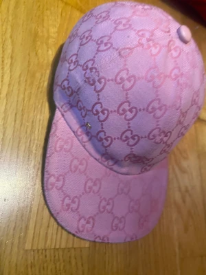 Rosa keps från Gucci med monogram - Säljer en rosa keps från Gucci med klassiskt GG-monogram över hela kepsen. Kepsen har böjd skärm och är tillverkad i tygmaterial. Perfekt för dig som vill sticka ut med en lyxig accessoar.