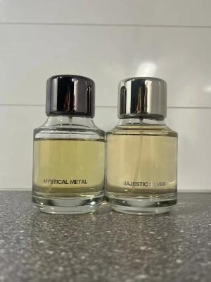 ZARA Mystical Metal & Majestic Silver parfym - ZARA 2 stilrena parfymflaskor: Mystical Metal och Majestic Silver. Båda har rund, transparent glasflaska med metallfärgad kork – en i mörkgrått och en i silver. Parfymen har en ljusgul ton och flaskorna har en modern, minimalistisk design. STORA flaskor, luktar så gott men jag använder andra därför säljer jag. 
