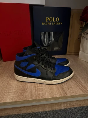 Svarta och blåa Air Jordan 1 Low - Säljer dessa balla och eftertraktade Nike Air Jordans och Mid i modellen black hyper royal, några få defekter som visas i bild men i helhet är dom i bra skick! 