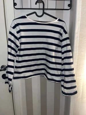 Randig långärmad topp från 157 - Säljer en klassisk långärmad topp från 157 i vitt och marinblått med horisontella ränder. Toppen har en rak passform och är tillverkad i mjuk bomull, perfekt för en avslappnad och stilren look.