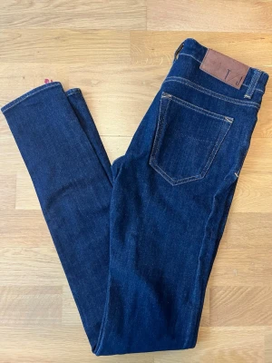 Mörkblå skinny jeans med läderpatch tiger of Sweden - Snygga mörkblå skinny jeans med klassisk femficksdesign och kontrastsömmar. Jeansen har en brun läderpatch i midjan och smal passform hela vägen ner. Perfekta för en trendig och stilren look.