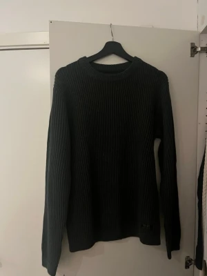 Svart ribbstickad tröja - En svart ribbstickad tröja med rund hals och långa ärmar. Tröjan har en enkel och stilren design, perfekt för lager-på-lager och passar till det mesta. Materialet ser ut att vara mjukt och bekvämt, vilket gör den skön att bära under kyliga dagar.