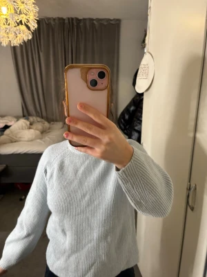 Ljusblå stickad tröja - Ljusblå stickad tröja med rund hals och långa ärmar. Tröjan har ett klassiskt ribbstickat mönster och är gjord i mjukt material som känns skönt mot huden. Perfekt för att hålla sig varm under kyliga dagar.