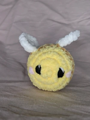 Gullig virkad bi 🐝 - Söt handgjord bi virkad i mjukt gult, brunt och vitt garn. Biet har vita vingar, svartvita ögon och små rosa kinder. Den är 6 cm bred och 6 cm hög. Perfekt som dekoration eller present till någon som gillar söta saker.