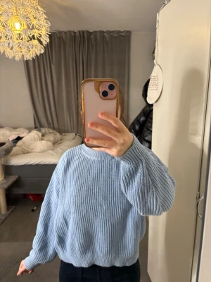 Ljusblå stickad tröja från 157 - Mysig ljusblå stickad tröja från 157 i storlek XS. Tröjan har en relaxed fit med rund halsringning och ribbstickade muddar vid ärmslut och nederkant. Perfekt för lager på lager och chill dagar.