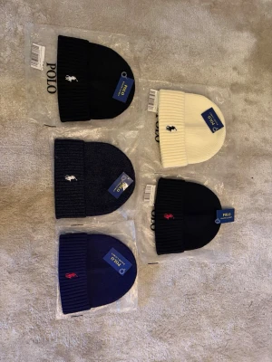 Polo Ralph Lauren - Snygg mörkblå ribbstickad mössa från Polo Ralph Lauren med klassisk vit broderad logga framtill. Mössan har uppvikt kant och är tillverkad i mjukt, värmande material. Perfekt accessoar för kalla dagar. 185 st. Än så länge så har 2 mössor sålts och de mössorna med enskilda bilder finns kvar. Om du vill köpa flera så kan priset även diskuteras billigare. 