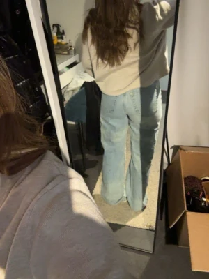 Ljusblå slitna jeans med raka ben - Säljer ett par ljusblå jeans med raka ben och slitningar vid knäna. Jeansen har klassisk femficksdesign och hög midja. Perfekta för en avslappnad och trendig look.