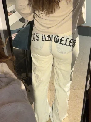 Ljusblå jeans med tryck bak - Säljer ett par ljusblå raka jeans med coolt svart 'LOS ANGELES'-tryck över bakfickorna. Jeansen har hög midja och klassisk femficksdesign. Materialet är denim i bomull och passformen är relaxed och trendig.