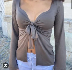 Brun långärmad topp med knyt - Trendig brun långärmad topp med djup v-ringning och knyt framtill. Toppen har en croppad passform och är tillverkad i mjukt material som sitter snyggt på kroppen. Perfekt för dig som vill ha en stilren men ändå unik look. Nypris 393 