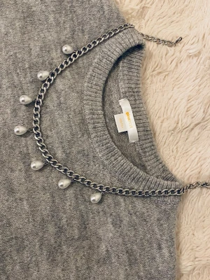 Kedjehalsband med droppformade pärlor - Snyggt halsband i silverfärgad metall med droppformade vita pärlor som hänger längs hela kedjan. Kedjan har en klassisk länkdesign och justerbart lås. Perfekt för dig som vill ha en trendig accessoar med lite edge och pärldetaljer.