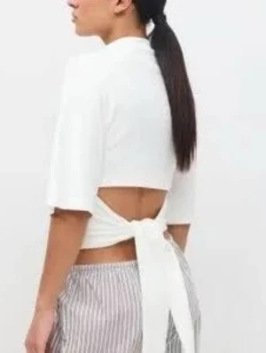 Vit omlott topp med knytband - Snygg vit omlott topp med knytband i ryggen och korta ärmar. Toppen har öppen rygg och är perfekt för att skapa en trendig look. Passformen är normal och materialet ser ut att vara bomull.