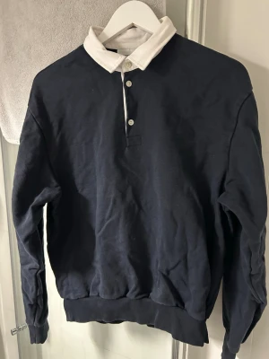 Mörkblå rugbytröja från Weekday - Snygg mörkblå rugbytröja från Weekday. Använd 2~3 gånger resten av tiden har den legat nedvikt i garderoben, där av att den ser skrynklig ut. Den är liten i storleken så kommer sätta den som XS även fast den är S