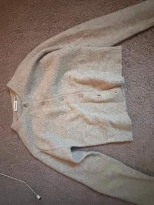 Beige kofta från Kappahl XS - Mysig beige kofta från Kappahl i storlek XS. Koftan har rund halsringning, knappar framtill och ribbade muddar vid ärmslut och nederkant. Perfekt för lager på lager och enkel att matcha med olika outfits.