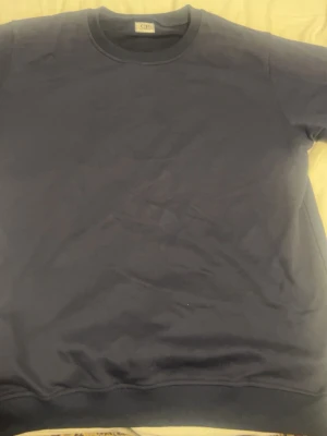 Mörkblå sweatshirt från Cp company - En enkel och stilren mörkblå sweatshirt från CP Company. Tröjan har rund halsringning, långa ärmar och en liten ficka med knapp på ena ärmen. Tillverkad i mjukt bomullsmaterial som känns skönt mot huden. Perfekt för en avslappnad look.