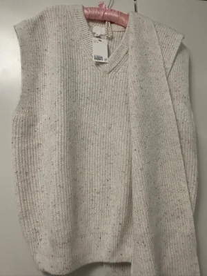 Ljus stickad väst med v-ringning - Säljer en ljus, ribbstickad väst med v-ringad hals. Västen är ärmlös och har en avslappnad passform. Perfekt att styla över en skjorta eller t-shirt för en trendig lager-på-lager-look.