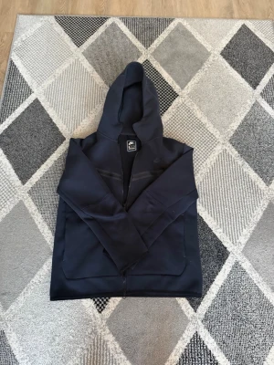 Mörkblå hoodie från Nike XXL - Snygg mörkblå hoodie från Nike i storlek XXL. Hoodien har dragkedja framtill, två stora fickor och en klassisk huva. Perfekt för en avslappnad streetstyle-look. Tillverkad i mjukt material som känns skönt mot huden.