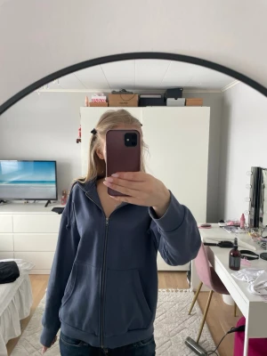 Blå zip-hoodie med huva - Säljer en blå hoodie med dragkedja och huva. Tröjan har ribbade muddar vid ärmslut och nederkant, samt två fickor framtill. Perfekt för chill dagar och enkel att matcha med jeans eller joggers.