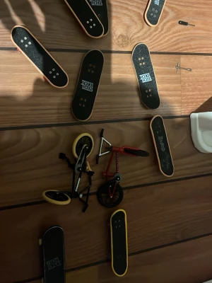 Tech Deck fingerboards och minicyklar - Samling med flera Tech Deck fingerboards i svart med träkanter samt två små BMX-cyklar i plast och metall. Tillbehör och reservdelar som verktyg och hjul ingår, allt i en praktisk plastlåda. Perfekt för dig som gillar fingerboards och miniatyrtricks.