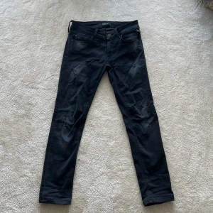 Svarta Replay jeans skinny fit - Snygga svarta jeans från Replay med skinny passform och klassisk femficksdesign. Jeansen har diskreta slitningar och svarta sömmar, samt Replay-logga på bakfickan. Perfekta för dig som gillar en smal siluett och stilren look. Jeansen har en liten defekt vid gylfen som man kan se på bilden.