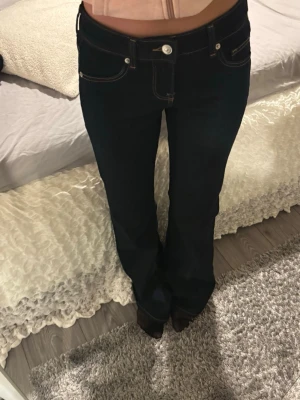 flared low jeans mörkblå - Slutsålda mörkblå bootcut jeans med klassiska fem fickor och kontrastsömmar. Jeansen har låg midja och stängs med knapp och dragkedja. 