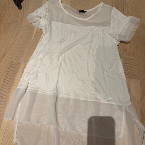 Vit transparent topp från Lindex - Säljer en vit topp från Lindex med transparenta partier och korta ärmar. Toppen har en längre, luftig passform och rund halsringning. Perfekt för lager-på-lager och en stilren look.