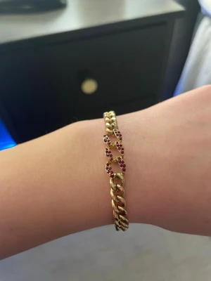 Guldarmband med röda stenar - Snyggt guldarmband med kedjelänkar där vissa länkar är dekorerade med små röda stenar som ger en lyxig och trendig känsla. Perfekt accessoar för att lyfta din stil med lite extra färg och bling.