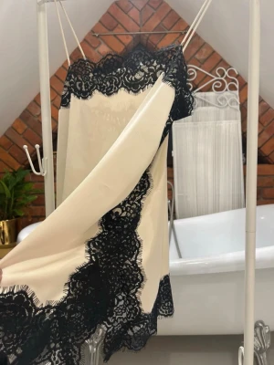 Champagnefärgad klänning med spets - Säljer en champagnefärgad kortklänning med tunna axelband och breda svarta spetsdetaljer längs kanterna. Vet tyvärr ej märket då jag köpte på Vinted och den saknar lapp men ser exakt ut som den från Zara. Aldrig använd.