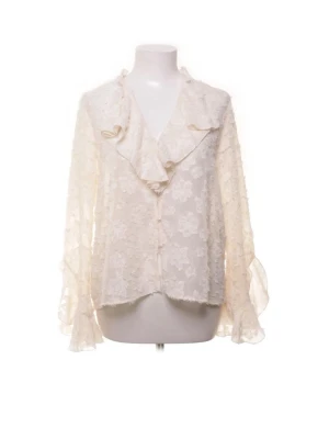 Vit spetsblus med volangkrage - Crémevit blus i spets med blommigt mönster och volangkrage. Blusen har långa, transparenta ärmar med volangdetaljer vid ärmslut. Är i storlek S och köptes på Sellpy, men har aldrig kommit till användning