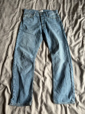 Ljusblå raka jeans från jack and jones - Säljer ett par klassiska ljusblå jeans från jack and jones med rak passform och fem fickor. Jeansen har normal midja, dragkedja och knappstängning samt Levi's ikoniska läderpatch bak i midjan. Tillverkade i slitstark denim av bomull.