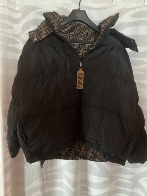 Svart pufferjacka  - Säljer en svart pufferjacka  med ikoniskt FF-mönstrat foder och detaljer. Jackan har dragkedja framtill med Fendi-logga på zip-pullern och hög krage. Oversized passform och tjock vaddering gör den perfekt för kalla dagar.