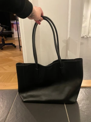 Svart handväska i konstläder - Stilren svart väska i konstläder. Mellanstor! Kommer ej ihåg var jag köpte denna!