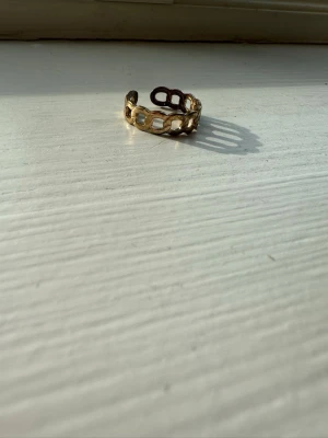 Guldig ring med kedjemönster - Snygg guldig ring med öppningsbar design och ett coolt kedjemönster runt hela ringen. Perfekt för dig som gillar statement-smycken och vill ha något unikt på fingret. Materialet ser ut att vara metall med en blank finish.