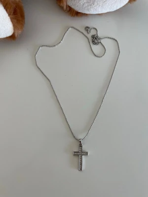 Silverfärgat halsband med korshänge/ silver guldpläterad  - Snyggt halsband i silverfärg med ett korsformat hänge dekorerat med små glittrande pärlor. Kedjan är tunn och har ett klassiskt lås. Perfekt accessoar för dig som gillar stilrena smycken med lite extra bling.