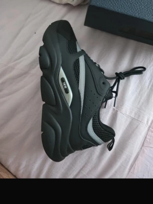 Svarta Dior sneakers - Snygga svarta Dior sneakers med chunky sula och gråa detaljer. Skorna har meshpaneler för extra ventilation, perforerade partier på sidan och en tydlig Dior-logga på sulan. Klassisk snörning och sportig design som sticker ut. Alla tillbehör medföljer så som låda och dustbag!