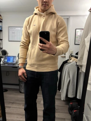 Beige hoodie från Tommy Hilfiger - Snygg beige hoodie från Tommy Hilfiger med liten broderad logga på bröstet. Klassisk känguruficka framtill, ribbade muddar och justerbar huva med dragsko. OBS! Är extra stor i storlek för att vara S så den är mer baggy.