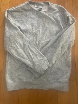 Grå sweatshirt från Weekday - En stilren grå sweatshirt från Weekday i mjukt bomullsmaterial. Klassisk rund halsringning, långa ärmar och ribbade muddar vid ärmslut och nederkant. Perfekt basplagg för en avslappnad look. Har endast använts en gång och passar för både killar och tjejer.       