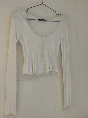 Vit långärmad topp med spetsdetaljer - Söt vit långärmad topp från Gina Tricot med spetskant runt ringningen och en liten rosett framtill. Använd få gånger.